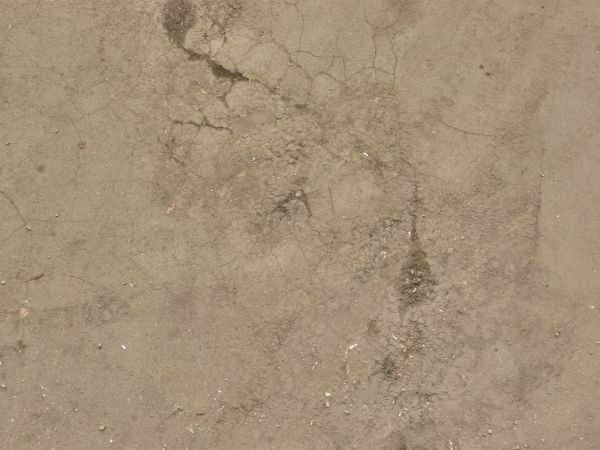 Brown asphalt texture with several small cracks, covered by a fine layer of sandy dirt.